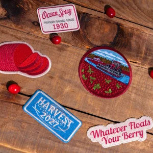 Embroidered Ocean Spray collectible patches and loose cranberries on a wooden surface