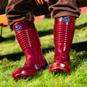 Person wearing glossy red Ocean Spray rain boots on the grass