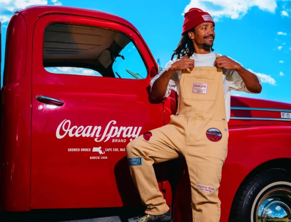 Model in tan Ocean Spray Waderalls and red beanie beside a branded red truck